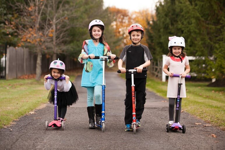 group of young children riding manual kick scooters that are ideal before an electric model