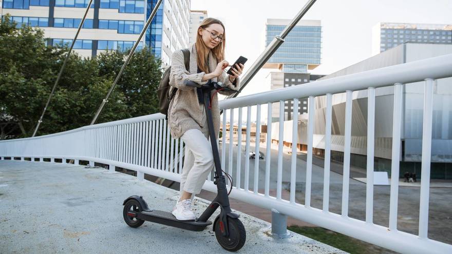 Woman standing with her Xiaomi scooter m365 and using her mobile phone