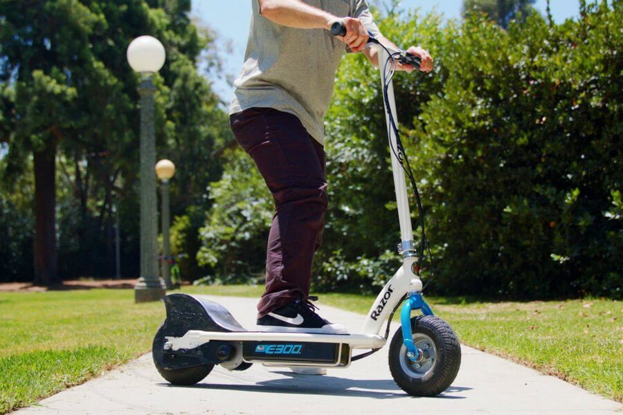 Side shot of the E300 by Razor held by rider on a pavement with grass and trees in the background.