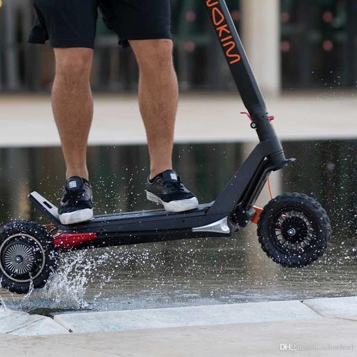 young man in shorts jumping on an Inokim scooter model OX black and orange