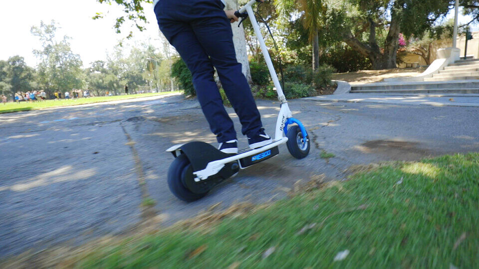 A blue and white e300 E-scooter leaning left for a turn on a park pathway