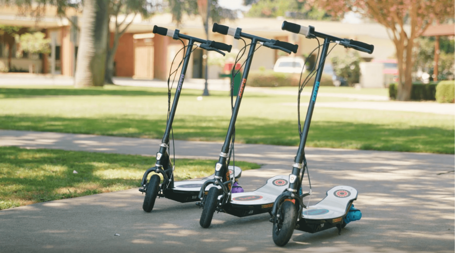 Set of 3 Razor electric scooters resting on stands in blue, orange and pick